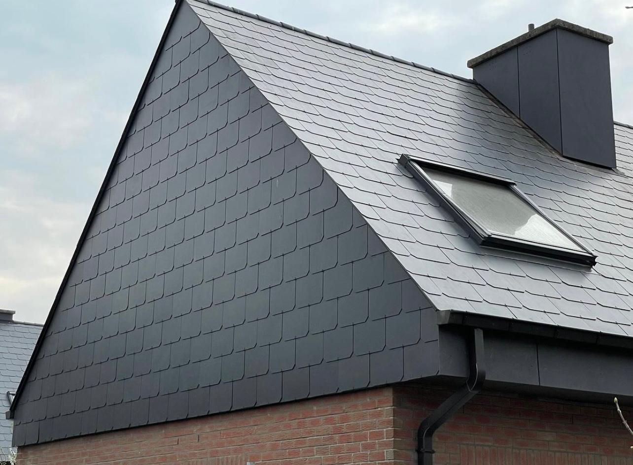 Detail van de dakpunt met strak geplaatste grijze kunstleien en een dakraam