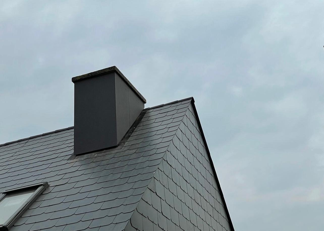 Detailopname van de schouwaansluiting en nokafwerking in grijze kunstleien